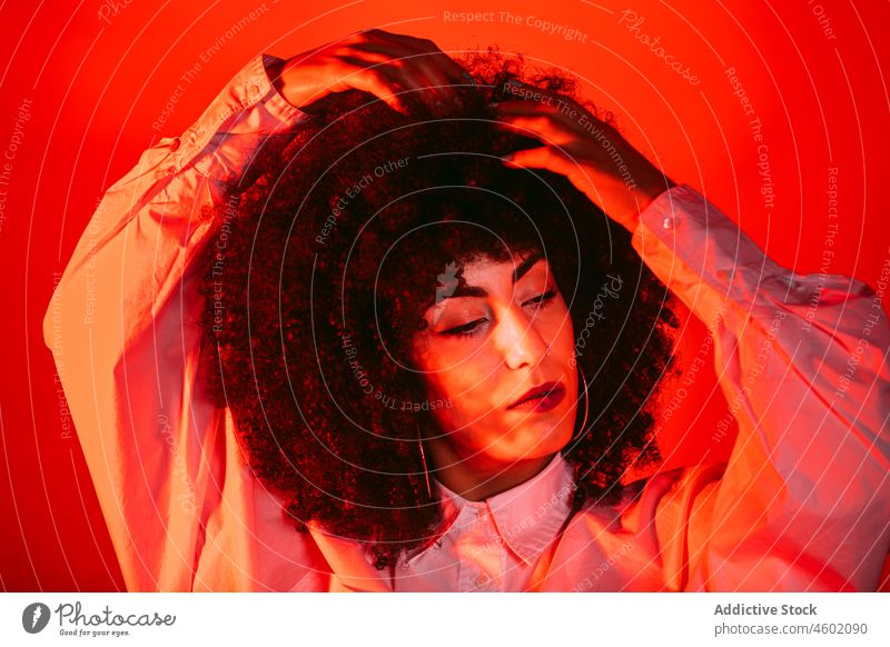Stilvolle ethnische Frau berührt Afro-Haar im roten Studio selbstsicher Windstille Haare berühren selbstbewusst Porträt Model Persönlichkeit traumhaft