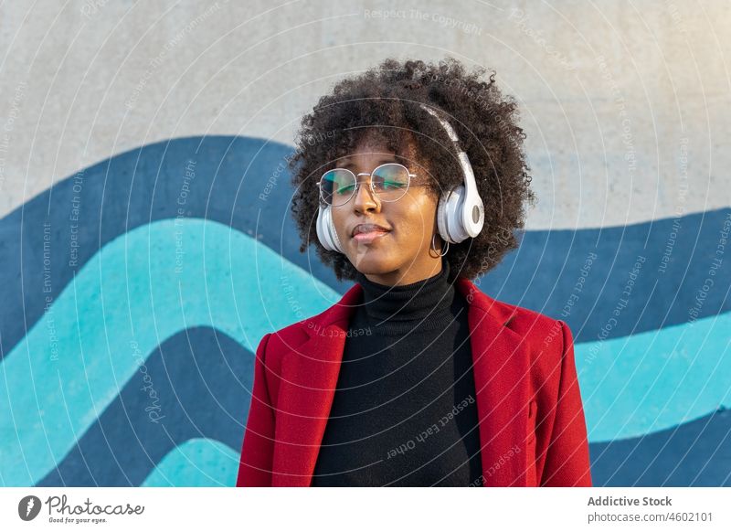 Stilvolle schwarze Frau mit Brille, die mit Kopfhörern Musik hört Afro-Look zuhören Rollkragenpulli Drahtlos Podcast Wiedergabeliste Apparatur Gerät Melodie