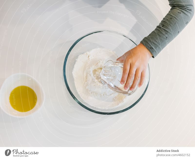 Erntekind gießt von Hand Wasser auf Mehl Kind Koch Bestandteil kulinarisch Gebäck vorbereiten Bäckerei eingießen Teig Schalen & Schüsseln Küche Erdöl Tasse