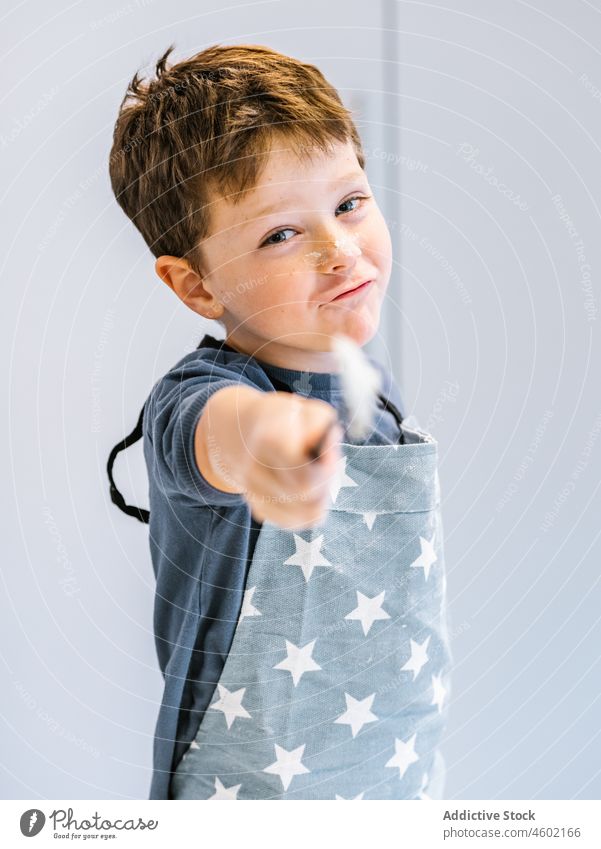 Niedlicher Junge mit Löffel beim Kochen in der Küche Kind Helfer heimisch Küchengeräte kulinarisch zu Hause Schürze dreckig Utensil lustig Lächeln vorbereiten