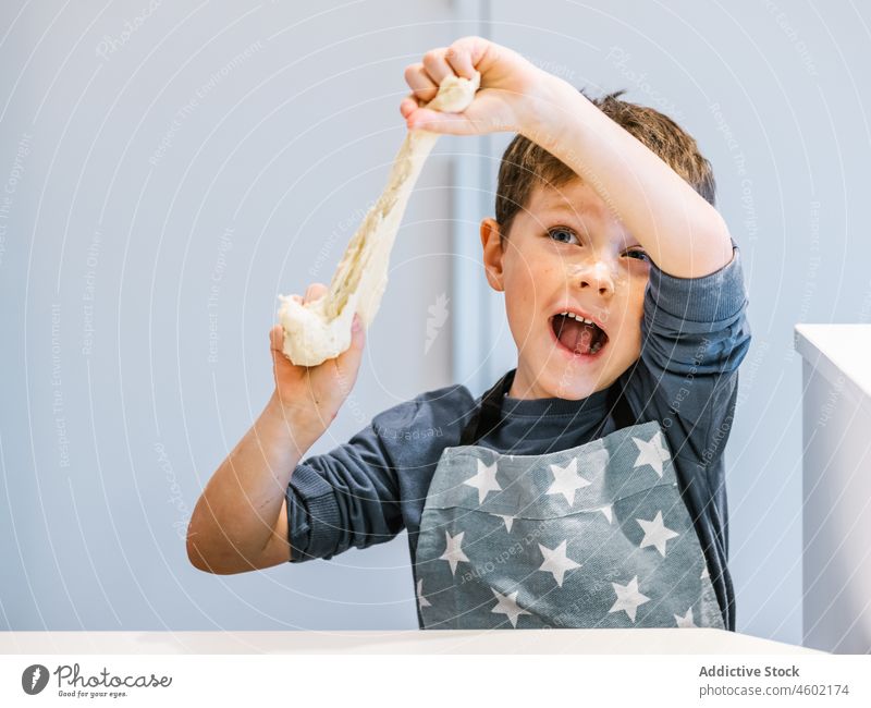 Fröhlicher Junge mit Teig in der Küche Koch Kind Teigwaren Mehl kneten Gebäck Spaß haben Helfer Träne Schürze Prozess backen Lebensmittel heimisch Küchengeräte