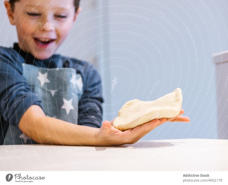 Niedlicher Junge in Schürze und mit Mehl im Gesicht bei der Zubereitung von Teig für Gebäck in der Küche zu Hause Koch Kind Teigwaren kneten Spaß haben Helfer