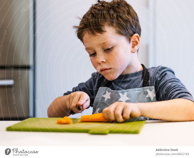 Konzentrierter Junge schneidet Karotte in der Küche Koch Möhre Kind geschnitten kulinarisch zu Hause Lebensmittel Helfer Scheibe vorbereiten Küchengeräte