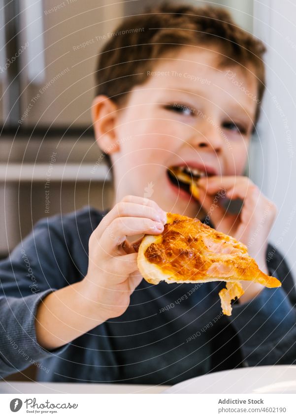 Fröhlicher Junge isst Pizza in der Küche essen Kind Küchengeräte heimisch zu Hause Lebensmittel Mahlzeit Spielfigur hungrig Vergnügen genießen Gebäck lecker