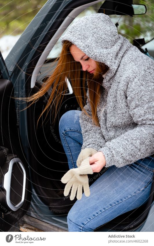 Frau sitzt auf dem Fahrersitz und zieht Handschuhe an PKW Winter Auto angezogen warme Kleidung Kapuze Autoreise geparkt festgeklebt lässig Fenster offen Tür
