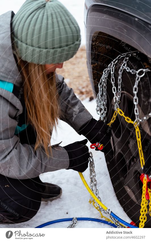 Frau legt Sicherheits-Schneekette in den Reifen eines Autos Rad PKW kalt Winter Winterzeit Verkehr Fahrzeug Frost angezogen festgeklebt anketten Autoreise