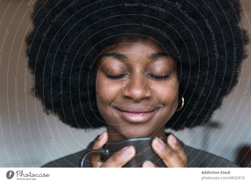 Positive schwarze Frau mit Heißgetränk Tasse Getränk Kaffee Afro-Look feminin Frisur verträumt Lächeln Vorschein Glück charmant brünett attraktiv heiter Inhalt