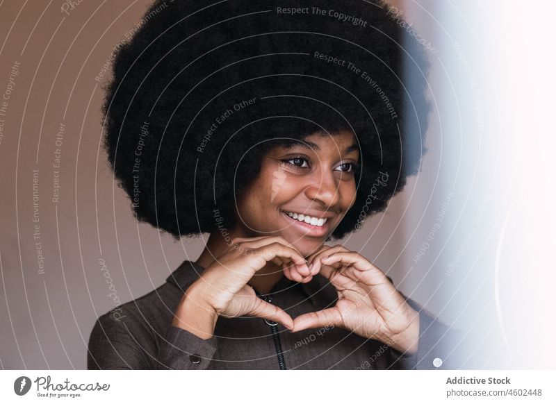 Lächelnde schwarze Frau zeigt Herzgesten durch Ringlampe Blogger gestikulieren Liebe Vlogger Freizeit Afro-Look Frisur feminin Vorschein Glück charmant brünett