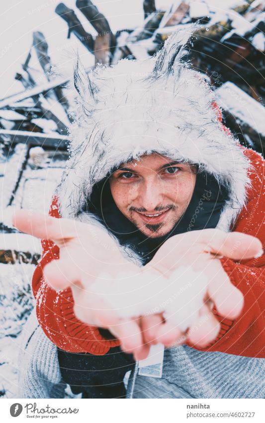 Junger Mann mit Pelzmütze und rotem Kapuzenpulli genießt einen verschneiten Tag Winter Schnee Spaß lustig genießen kalt frieren gefroren Leben Lifestyle weiß