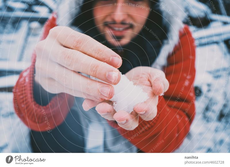 Junger Mann mit Pelzmütze und rotem Kapuzenpulli genießt einen verschneiten Tag Winter Schnee Spaß lustig genießen kalt frieren gefroren Leben Lifestyle weiß