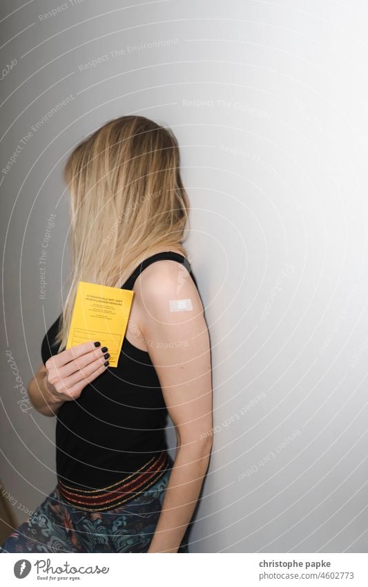 Frau mit Pflaster auf dem Oberarm hält Impfausweis in der Hand blond Impfung Corona Schutz albern Freude COVID Pandemie Corona-Virus Gesundheit Schützen