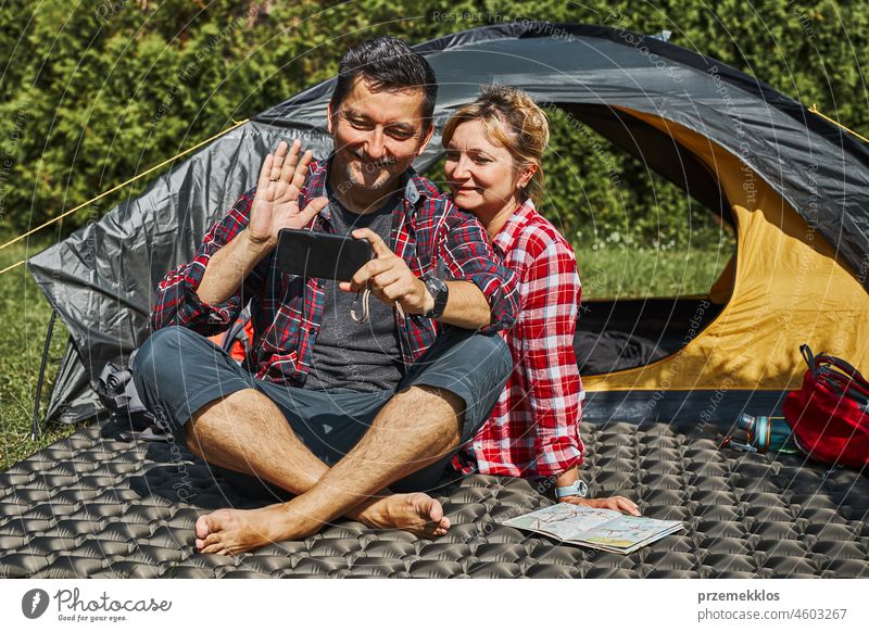 Ein Paar führt einen Videoanruf mit Freunden per Smartphone, während es im Zelt beim Camping sitzt. Menschen entspannen im Zelt während des Sommerurlaubs Urlaub