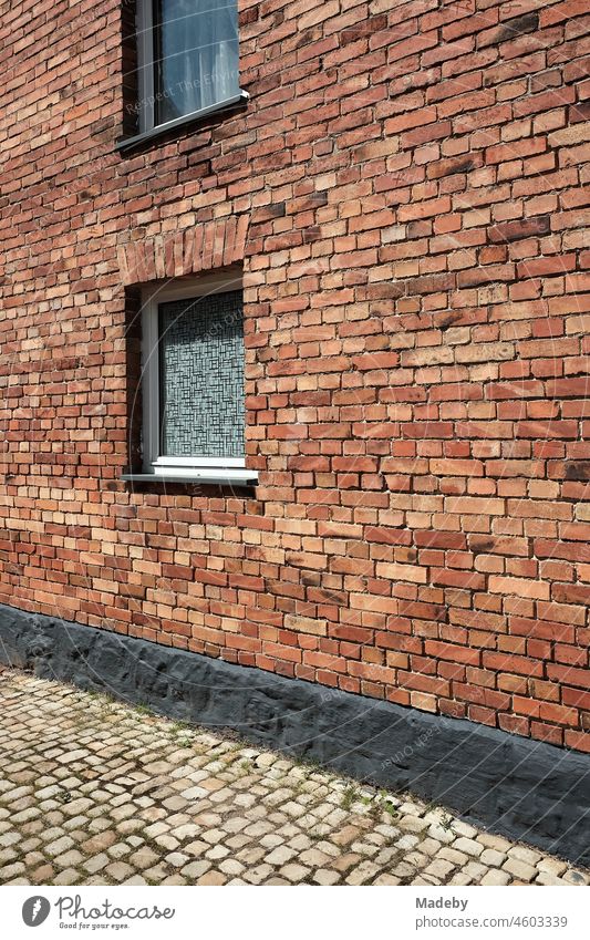 Fenster mit Riffelglas und Gardine in einer alter rotbraunen Klinkerfassade eines Bauernhaus mit grauem Kopfsteinpflaster im Sommer bei Sonnenschein in Alverdissen bei Barntrup in Ostwestfalen-Lippe