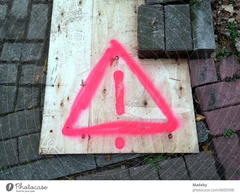 Holzplatte in Beige mit aufgemalten Achtung Warnzeichen in Pink über einer Baugrube auf dem Bürgersteig in Steinhude am Steinhuder Meer bei Wunstorf im Landkreis Hannover