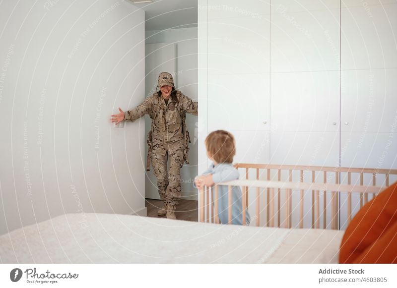 Militärfrau geht zu ihrem Sohn im Kinderbett Mutter Soldat Babybett Schlafzimmer back home Armee Lächeln Pflicht Junge Mutterschaft Patriotin niedlich Glück