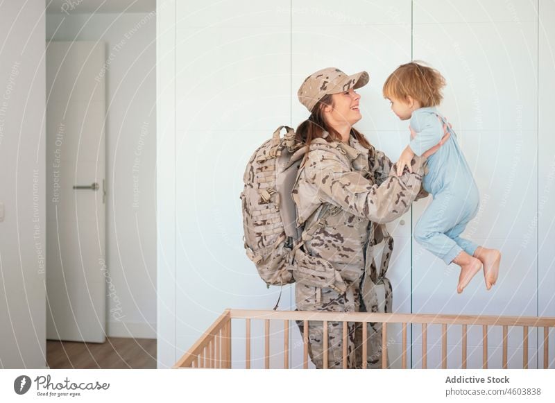 Fürsorgliche Militärfrau hält ihren Sohn Mutter Soldat Babybett Schlafzimmer Armee Pflicht Patriotin Junge Kind niedlich Frau Liebe Bett Zusammensein