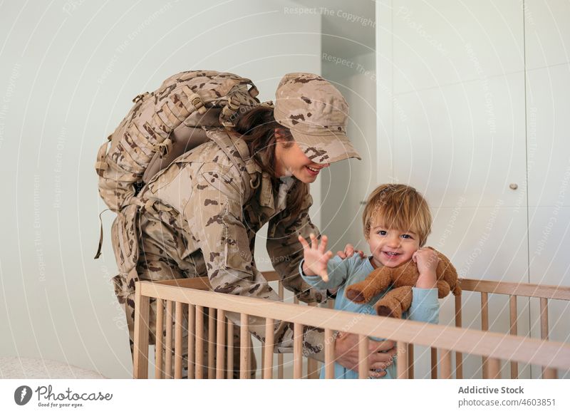 Fürsorgliche Militärfrau hält ihren Sohn Mutter Lächeln Soldat Babybett Schlafzimmer Armee Pflicht Patriotin Junge Kind niedlich Frau Liebe Bett Freude