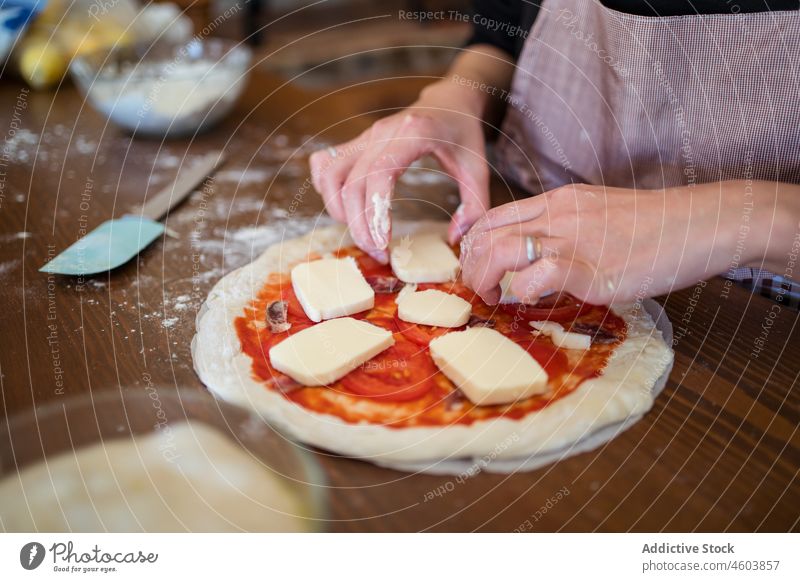 Gesichtslose Frau legt Käse auf rohe Pizza Koch Teigwaren Mozzarella Küche kulinarisch selbstgemacht Haushalt vorbereiten Küchenchef Tisch Schürze Prozess Licht