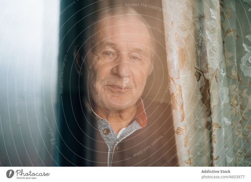 Ruhiger, nachdenklicher älterer Mann hinter dem Fenster Senior Lebensalter Raum Porträt Rentnerin Großeltern Einsamkeit allein heimwärts Gardine Licht