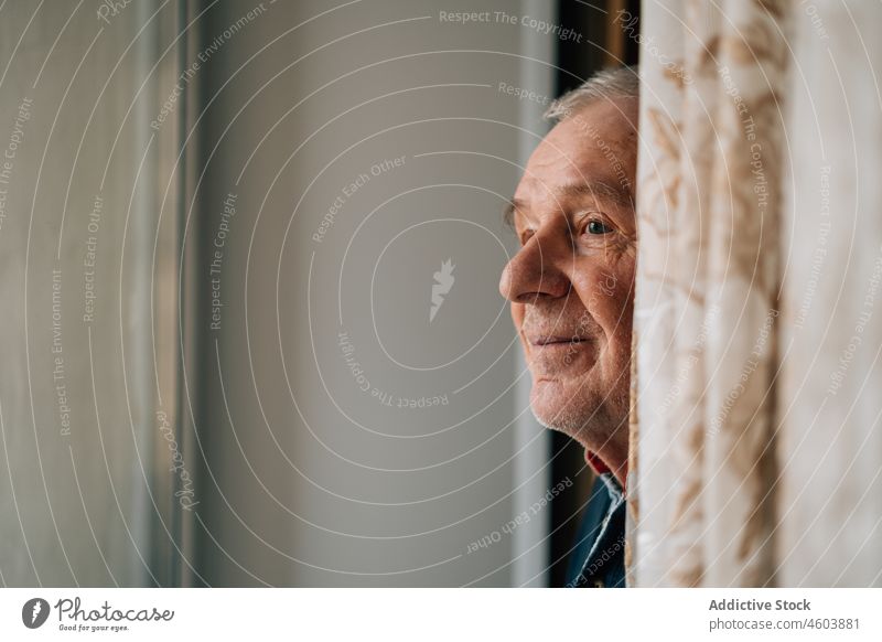 Älterer Mann steht am Fenster älter Senior Lebensalter Raum Porträt Rentnerin Großeltern Einsamkeit allein heimwärts Gardine Licht Windstille gealtert reif