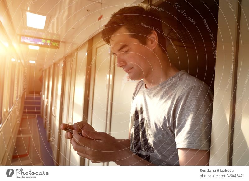 Alleinreise Erwachsener Mann reist allein mit dem Zug. Er steht in einem leeren Zugwaggon und schreibt eine SMS auf einem Telefon. Mit Smartphone-Technologie online Neue Normalität