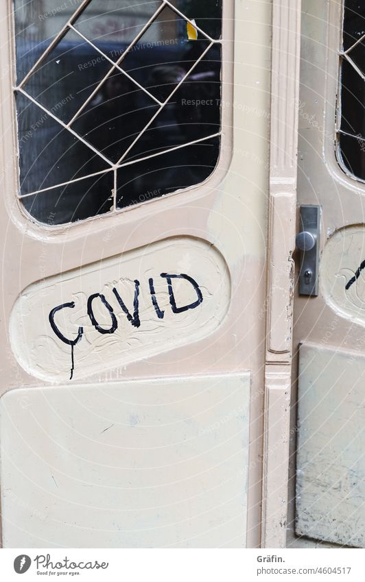 Covid steht auf einer alten Holztür - ist das eher eine Warnung als ein Hinweis? Graffiti Kritzelei Eingangstür hölzern verwohnt Wohnhaus Schriftzeichen