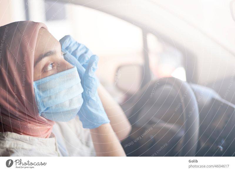 Muslimische Frau mit Gesichtsmaske und Handschuhen beim Autofahren PKW Mundschutz Coronavirus Pandemie jung muslimisch chirurgisch Arzt Hijab schützend