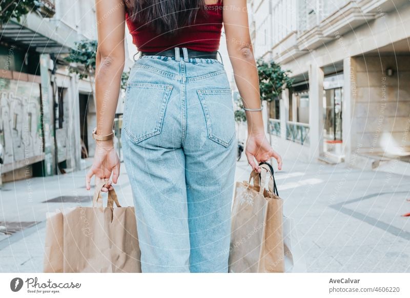 Rückansicht einer Frau, die Einkaufstüten hält und coole Klamotten trägt. Jeans und ein Top. Einkaufen Straße. Ändern und kaufen Geschenke Konzept. Person