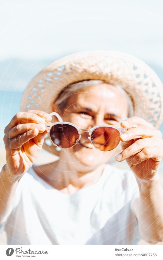 Glückliche ältere Frau lächelt, während sie die Sonnenbrille hält. Ruhestand ausruhen, neue gesunde Gewohnheiten, Reisen und tun Aktivitäten. Lächelnd und mit Spaß im Freien