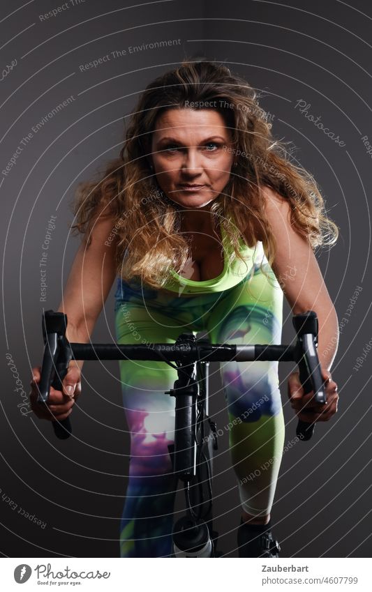 Sportliche schöne Frau trainiert auf Indoor-Rennrad sportlich trainieren Gute Vorsätze Heimtrainer Rennlenker grün neon Fitness Lifestyle Gesundheit Training