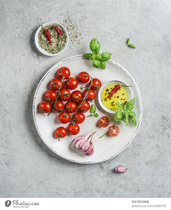 Frische leckere Zutaten: Tomaten, Schale mit Olivenöl, Kräutern, Knoblauch und grünem Salz mit Chilischote auf weißem Teller. Ansicht von oben frisch