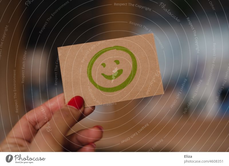 Frau hält Schild auf den ein positiv lächelnder Smiley gemalt ist gut Optimismus Freude Zufriedenheit grün Bewertung Stimmung gute stimmung Emoticon Gesicht