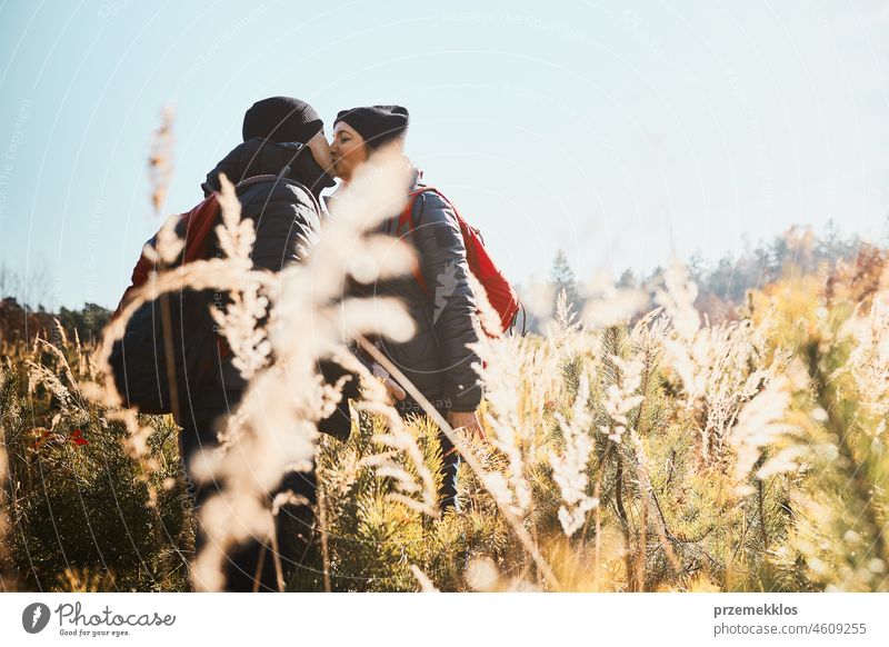 Paar teilt einen leidenschaftlichen Kuss während einer Urlaubsreise. Wanderer mit Rucksäcken stehen auf dem Weg. Menschen zu Fuß durch hohes Gras entlang Weg in der Wiese an einem sonnigen Tag