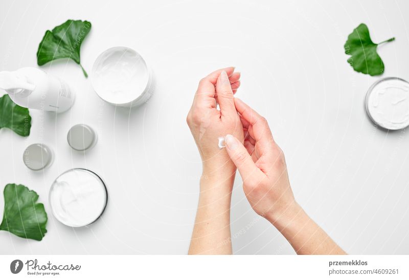 Frau trägt kosmetische, feuchtigkeitsspendende Handcreme auf. Kosmetische Produkte, grüne Blätter auf weißem Tisch. Spa, Maniküre, Hautpflege Konzept Pflege