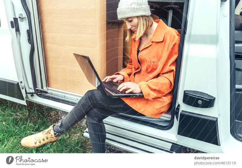 Frau bei Telearbeit in der Tür eines Wohnmobils sitzend Laptop Sitzen Kleintransporter Ausflug Fernarbeit genießend Natur Menschen heiter sich umschauen