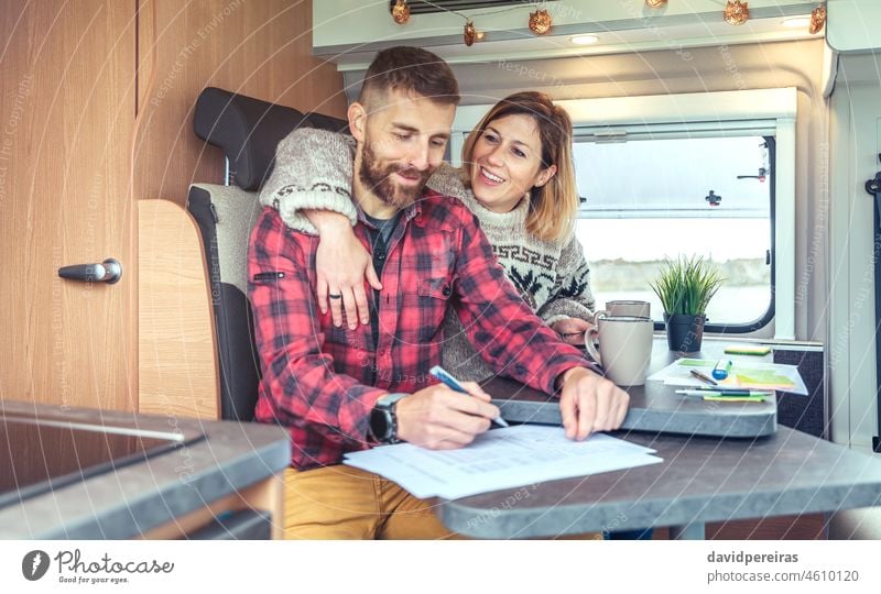 Ehepaar, das in einem Wohnmobil Telearbeit leistet Mann Paar Glück Kleintransporter Dokumente schreibend Fernarbeit Ausflug Menschen Job umarmend arbeiten