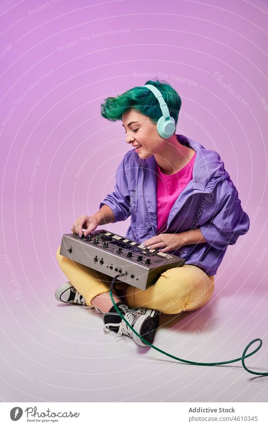 Positive Millennial-Frau mit Kopfhörern, die auf einem Keyboard-Controller spielt spielen Regler komponieren tausendjährig 80s Musik Musiker Stil Mode Design