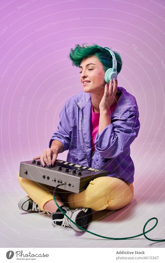 Zufriedene Millennial-Frau mit Kopfhörern, die auf einem Keyboard-Controller spielt spielen Regler komponieren tausendjährig 80s Musik Musiker Stil Mode Design