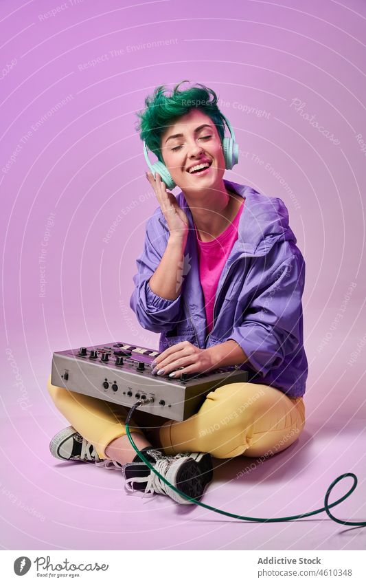 Positive Millennial-Frau mit Kopfhörern, die auf einem Keyboard-Controller spielt spielen Regler komponieren tausendjährig 80s Musik Musiker Stil Mode Design