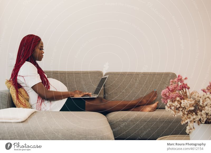 Schwarze schwangere Frau entspannt sich auf dem Sofa zu Hause mit seinem Laptop Unterleib Erwachsener Vorfreude Baby Bauch Geburt Business Pflege Chinesisch