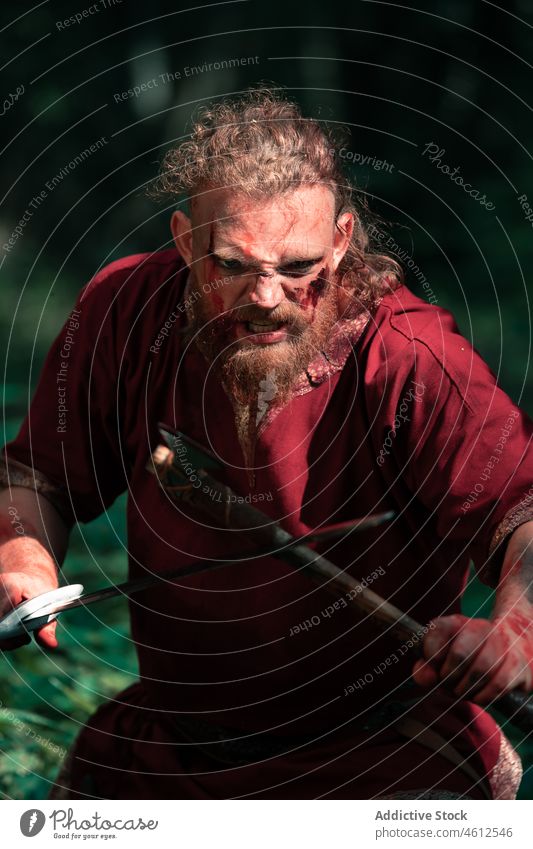 Aggressiver Wikinger mit Axt und Schwert kämpft im Wald Mann wütend Schutzschild schreien angriffslustig attackieren Nachstellung Schlacht männlich gewalttätig