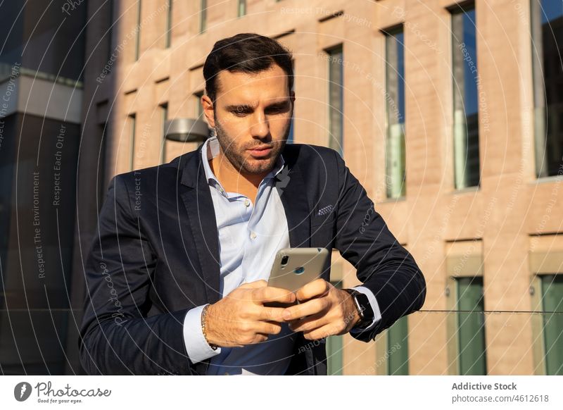 Geschäftsmann mit Smartphone im Anzug auf sonniger Straße Mann Unternehmer formal Großstadt urban männlich elegant brünett Glas Zaun Vollbart fettarm