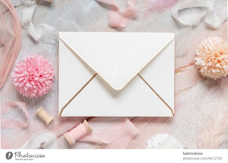Weißer Umschlag zwischen pastellfarbenen Blumen, Seidenbändern und Federn auf Marmor Hochzeit Kuvert Bändchen Murmel Attrappe rosa Draufsicht mädchenhaft