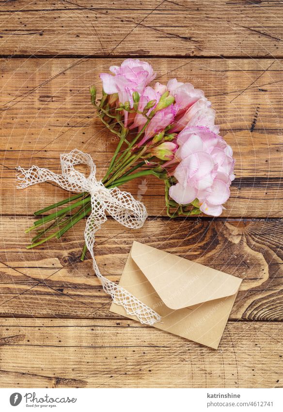 Blumenstrauß aus schönen Freesienblüten mit Band und Umschlag in der Draufsicht. Mockup auf Holztisch Feiertag hölzern Kuvert Attrappe rosa Geburtstag
