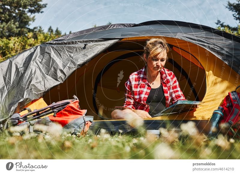 Frau plant nächste Reise, während sie mit Karte im Zelt sitzt. Frau entspannt im Zelt beim Camping im Sommerurlaub Urlaub Ausflug Abenteuer Campingplatz reisend