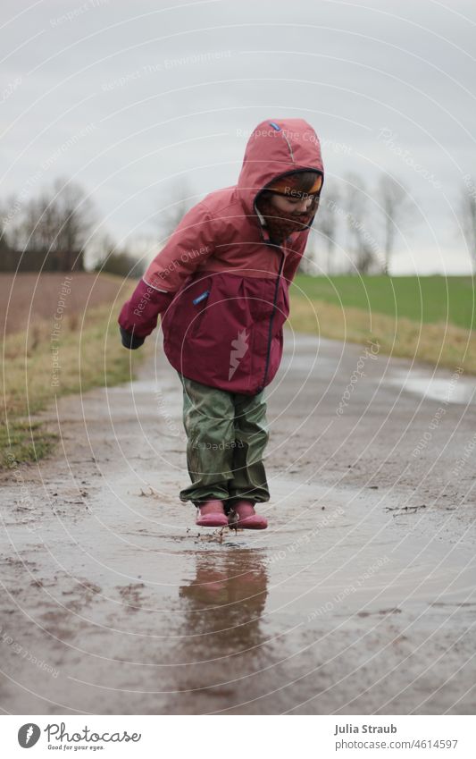Mädchen in Gummistiefeln schwebt über Riesenpfütze Pfütze Regenwetter regenkleidung matschhose Herbst Winter draußensein draußen spielen Kindheitserinnerung