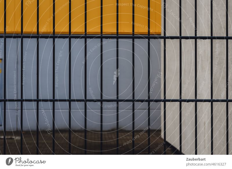 Zaun vor Wand und Hof, geometrisch in gelb und grau Gitter abstrakt rechteckig trist trostlos verschlossen geschlossen Sperre städtisch Stadt hässlich