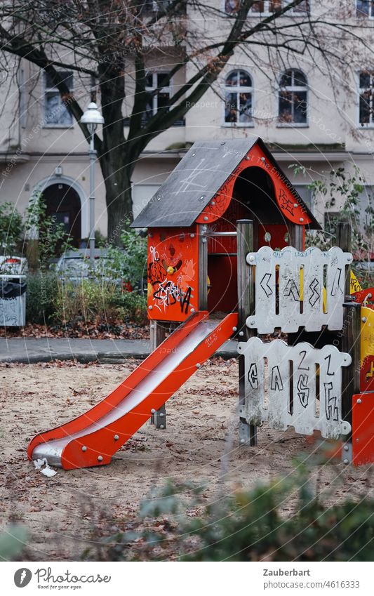 Spielplatz mit roter Rutsche in städtischer Umgebung Häuschen Zaun Sand Fassade Stadt Kindheit spielen Freude Spielzeug Grafitti urban Kindergarten Sandkasten