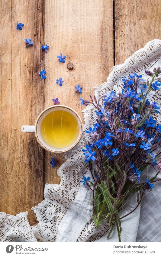 Blumenstrauß aus blauen Wildblumen und eine Tasse Tee auf einem Holztisch Nahaufnahme Frühstück Rahmen Flockenblume Design Kraut Kornblume Flora Frühling Tisch