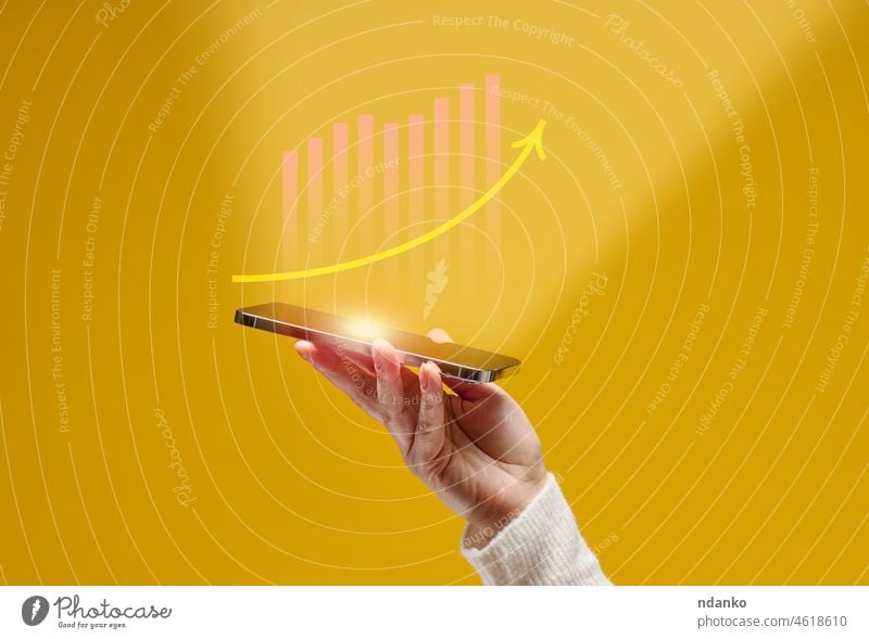 Frauenhand hält ein Smartphone mit holografischen Grafiken auf gelbem Hintergrund. Leistung, Wachstum, Erfolg Internet Analyse Analysieren Arme Pfeil Vorteil